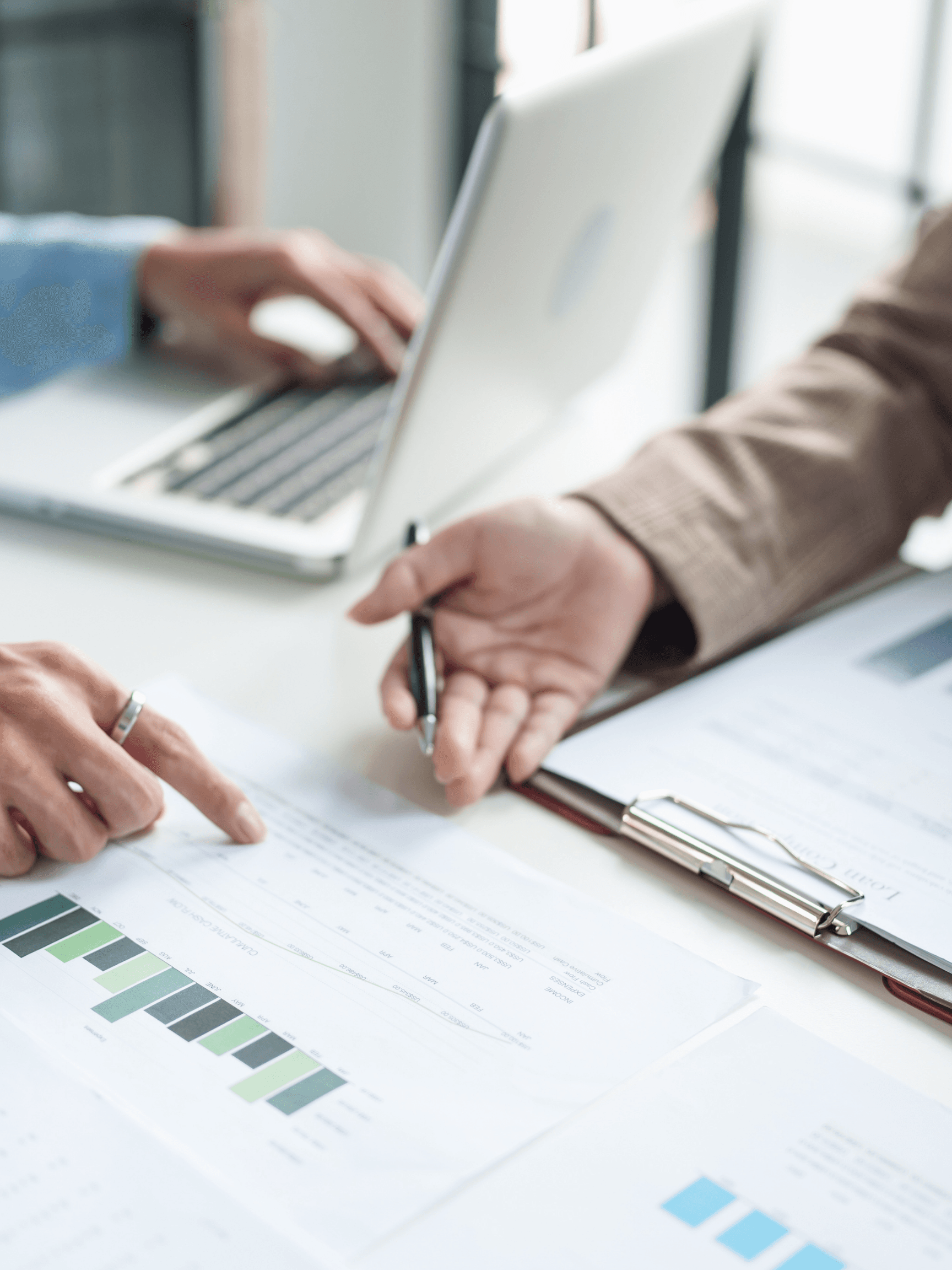 Professionals reviewing charts and financial documents on a desk beside a laptop