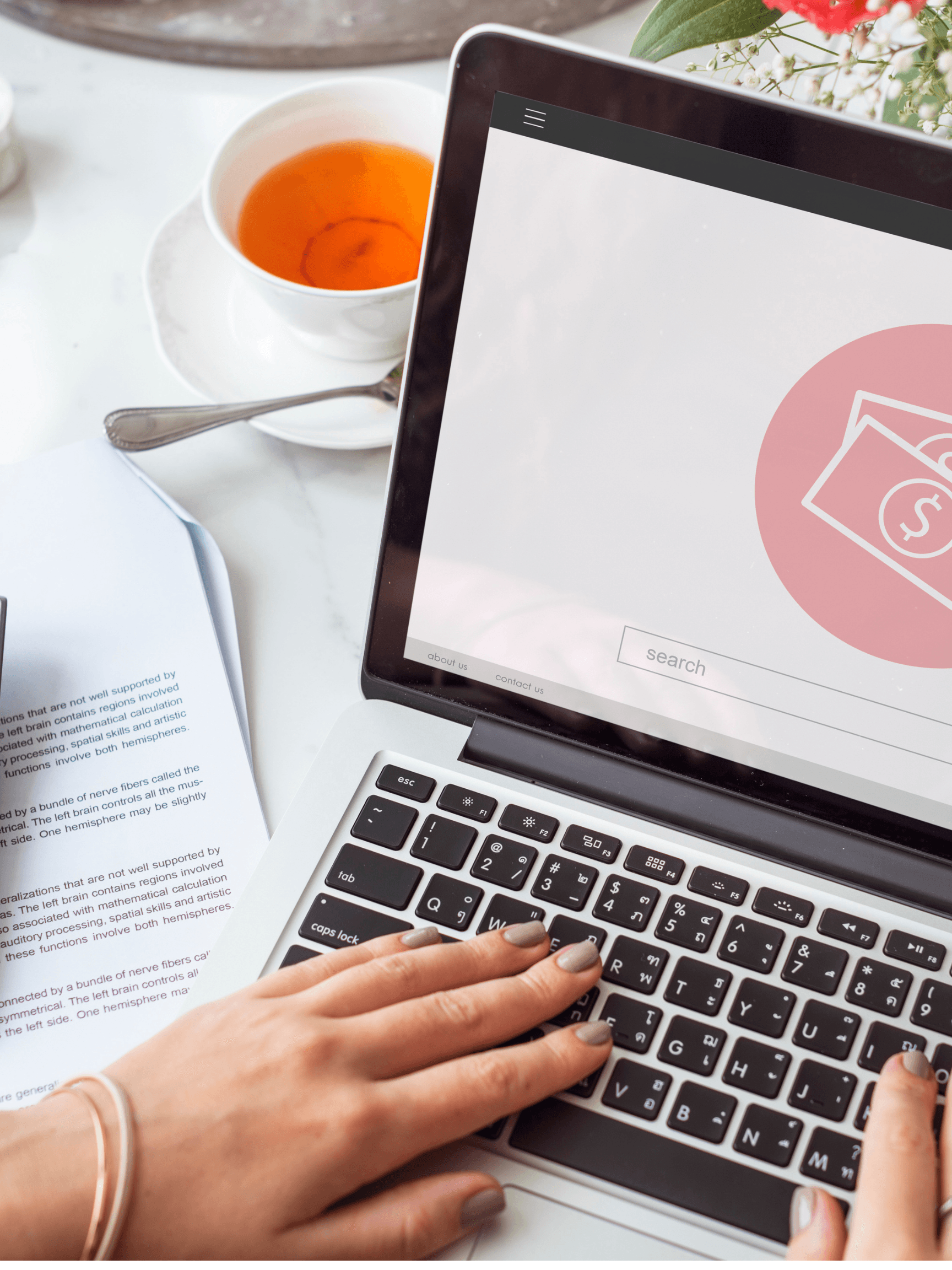 Person working on a laptop showing financial data, with tea and documents nearby